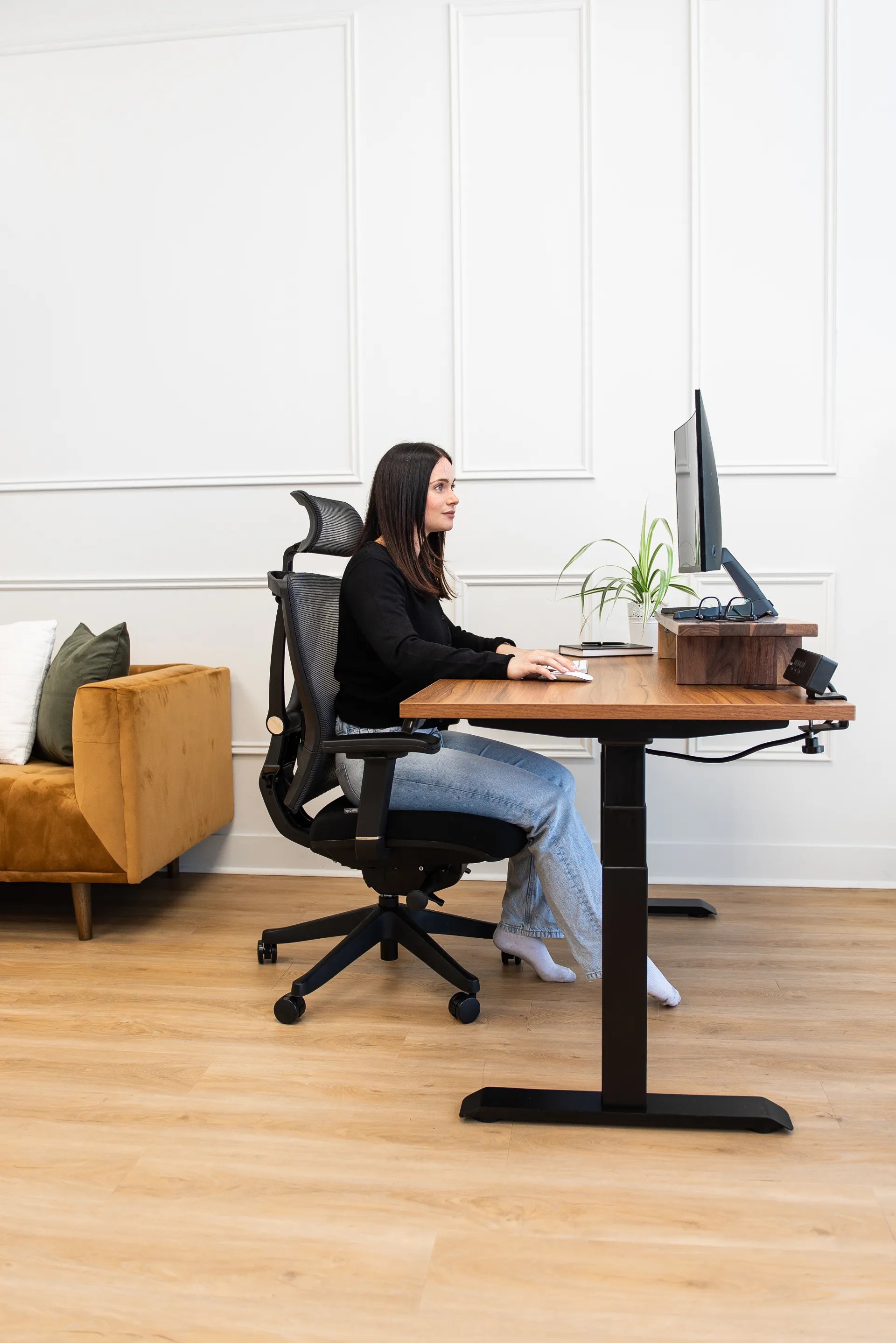 Woman seated in profile on a black Burotic ergonomic chair at a walnut adjustable desk