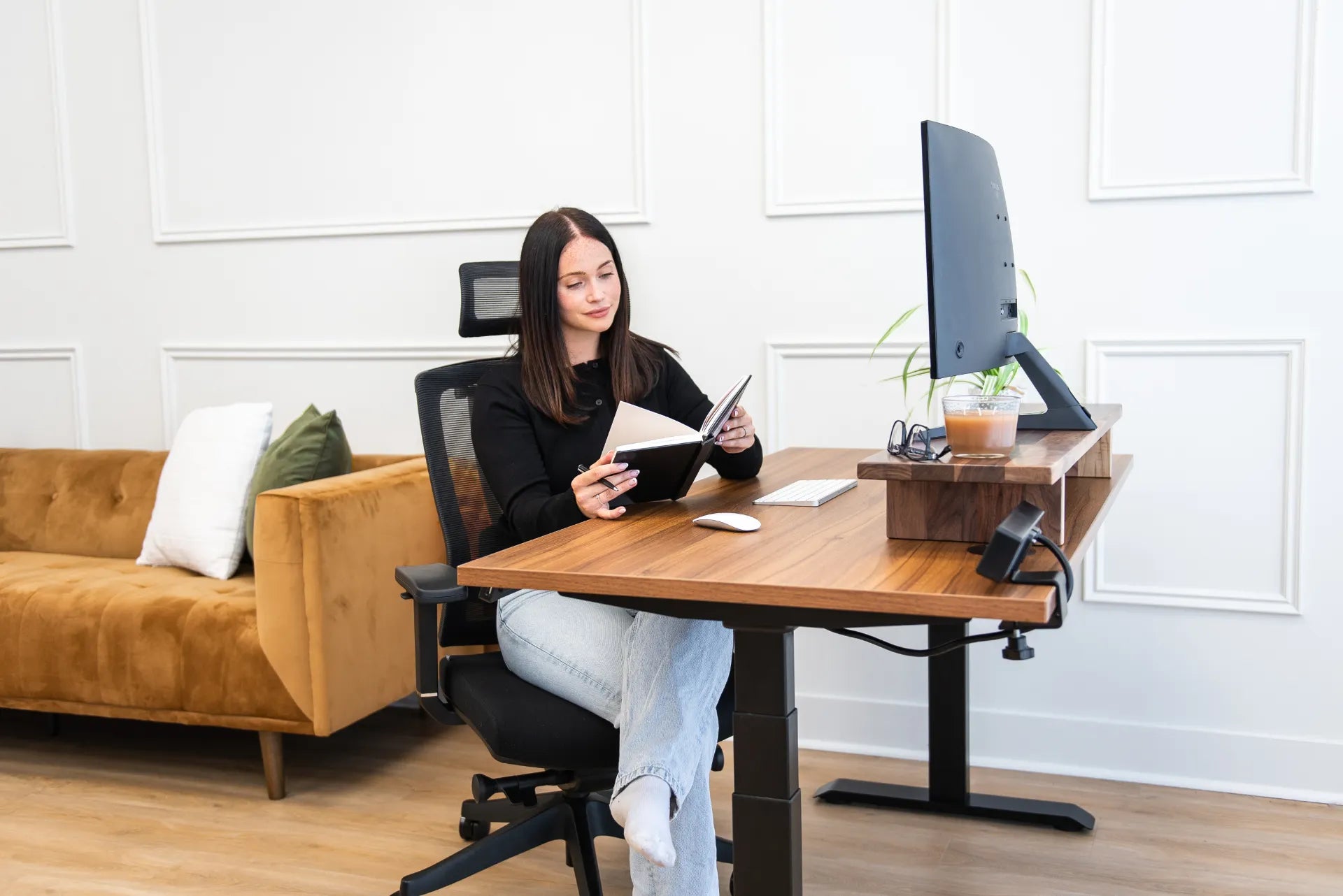 Woman seated in a black mesh ergonomic chair at a walnut adjustable desk