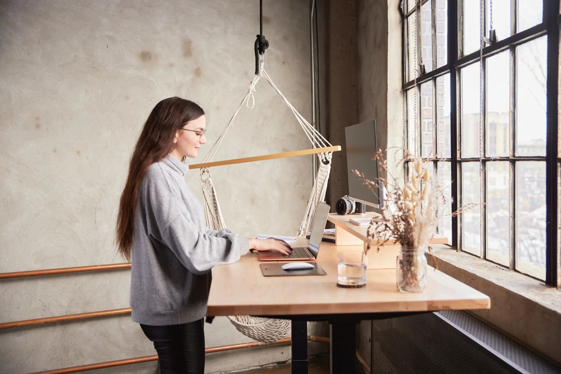 Woman working while standing at a Burotic desk beside a large industrial window