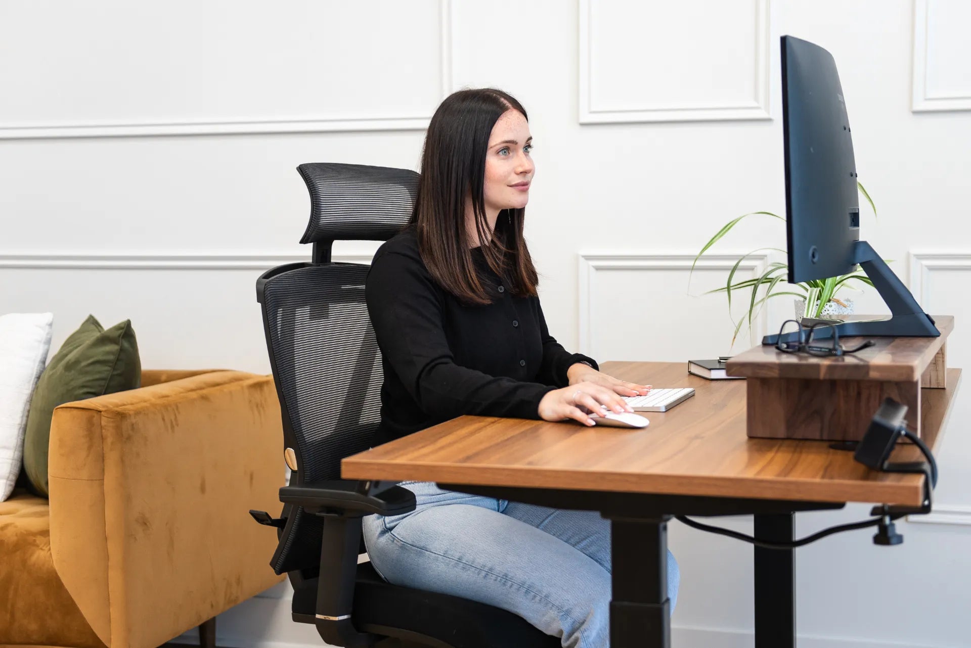 Woman seated upright on a black Burotic mesh chair at a walnut adjustable desk