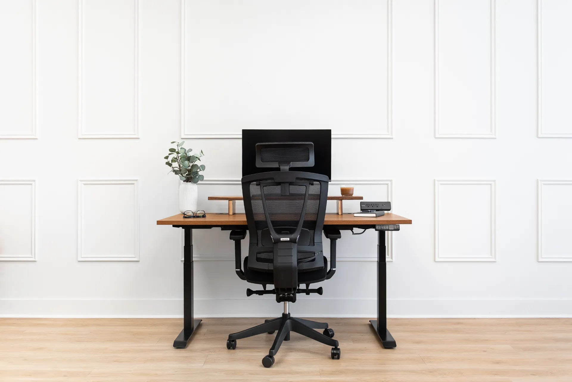Rear view of a black Burotic mesh chair showing the backrest and lumbar support at an adjustable desk