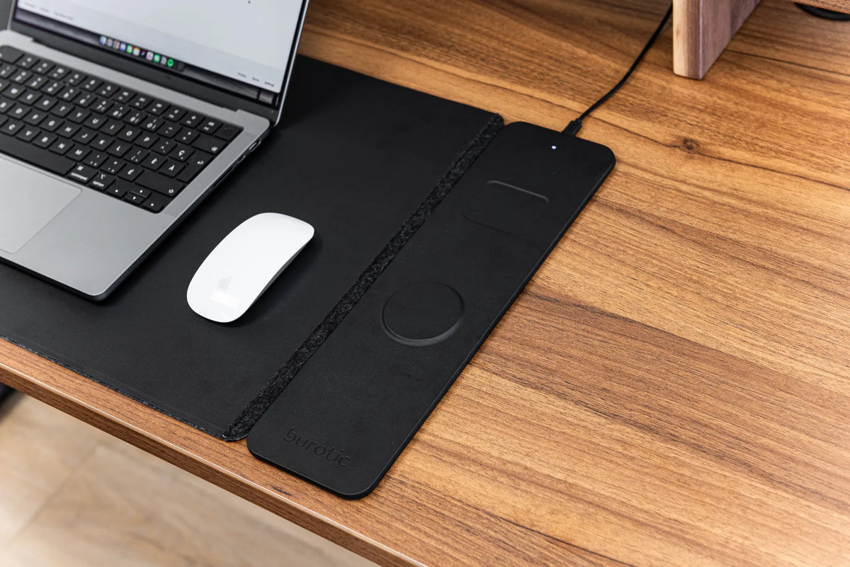 Black wireless charging desk pad with a laptop and white mouse on a wood desktop