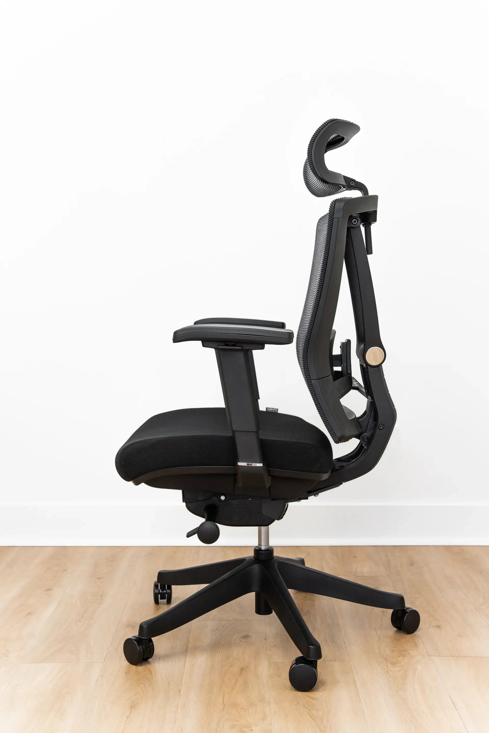 Side view of a black ergonomic chair showing the seat, controls, cylinder, base and casters