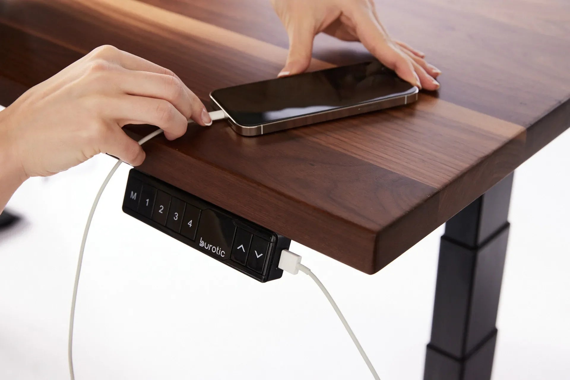 Phone cable connected to the USB port on a standing desk controller beside a walnut desktop