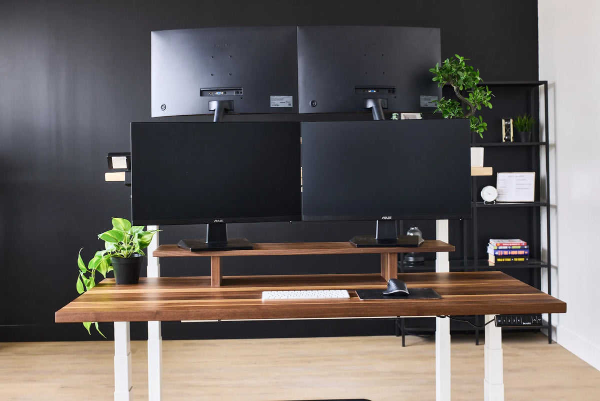 Walnut standing desk with four monitors arranged in two rows against a dark wall