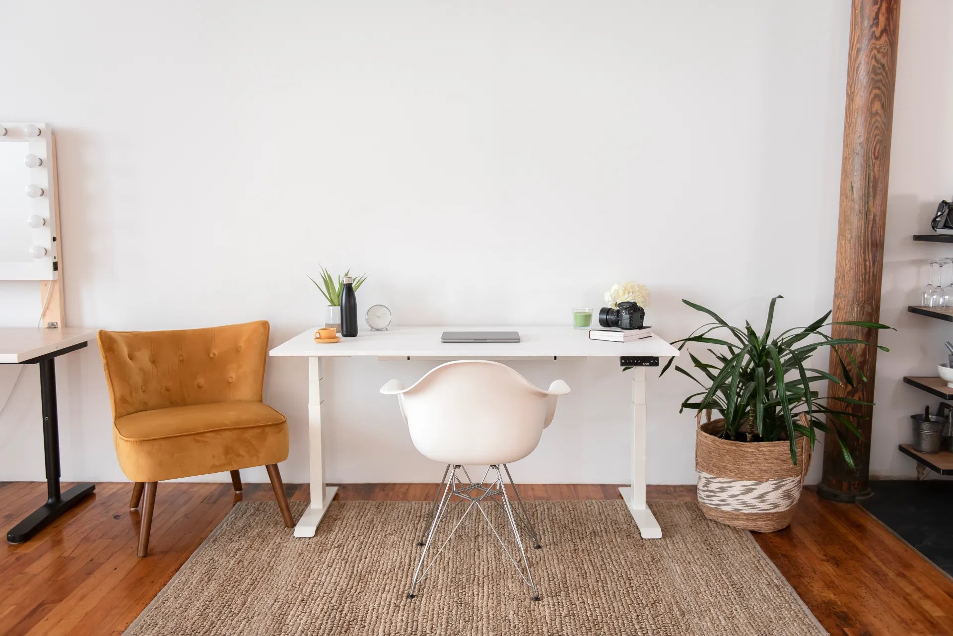 Bright home office with a white standing desk, mustard lounge chair, plants, rug and camera equipment