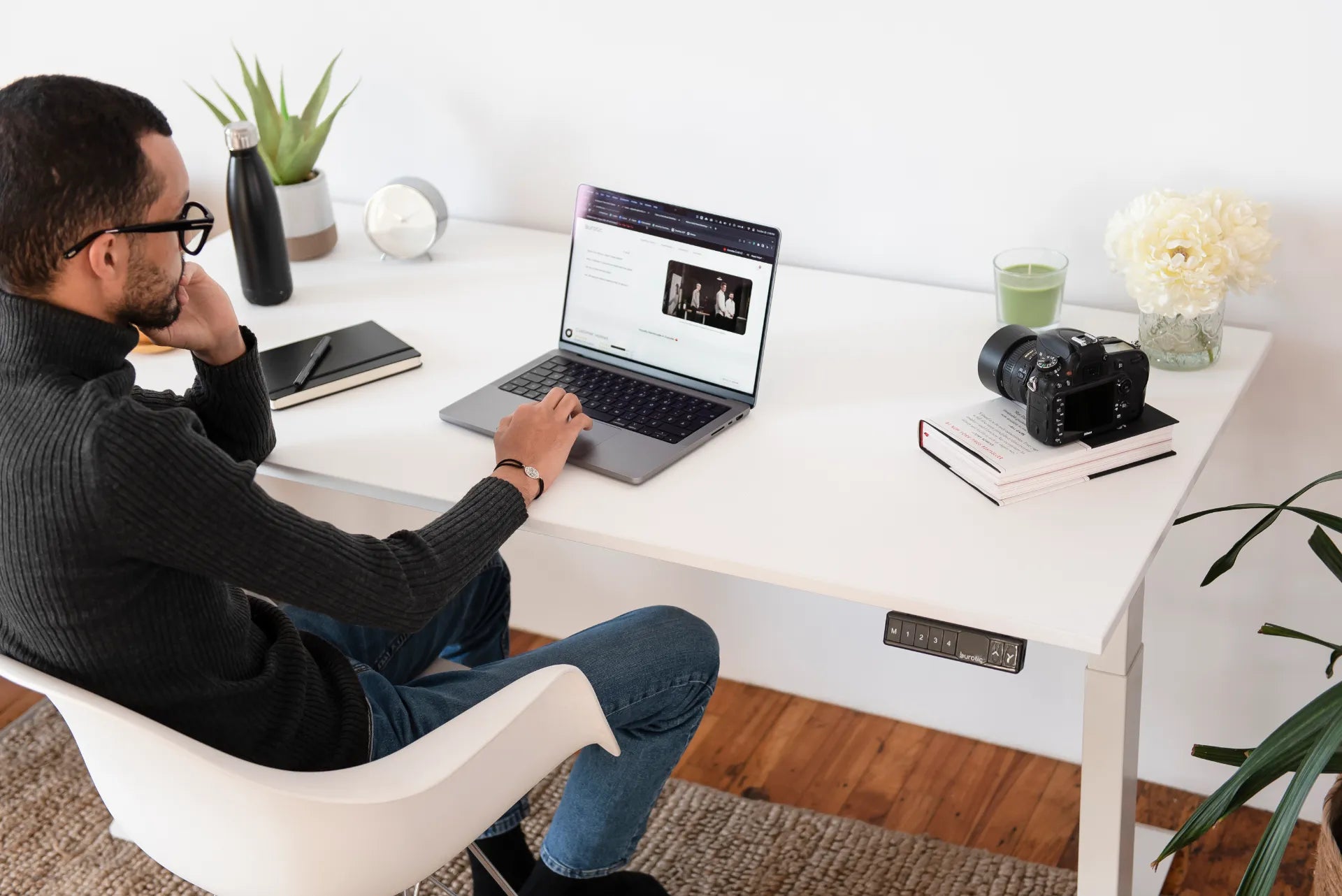 A person working on a laptop at a white standing desk in a bright home office