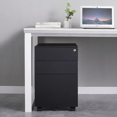 Black three-drawer filing cabinet next to a white desk with a laptop and books on a gray wall background.
